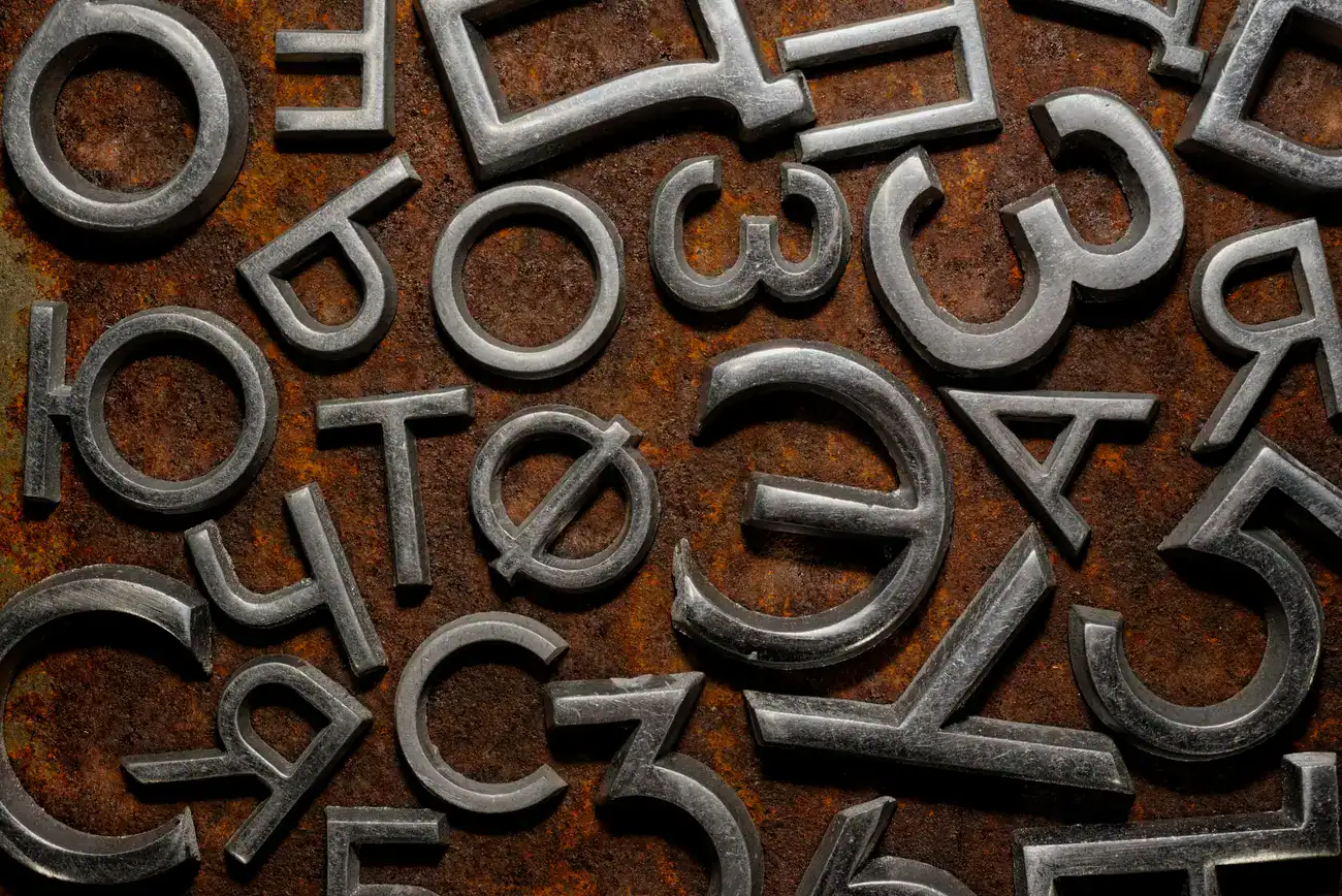 Metallic letters and numbers are scattered randomly on a rusty, textured surface.