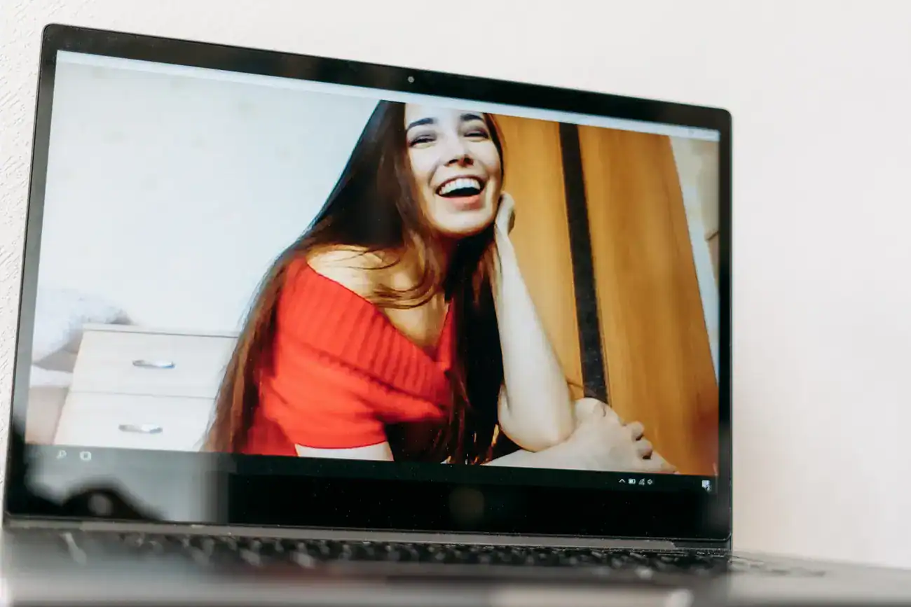 A laptop screen displays a video of a woman in a red top smiling and looking at the camera.