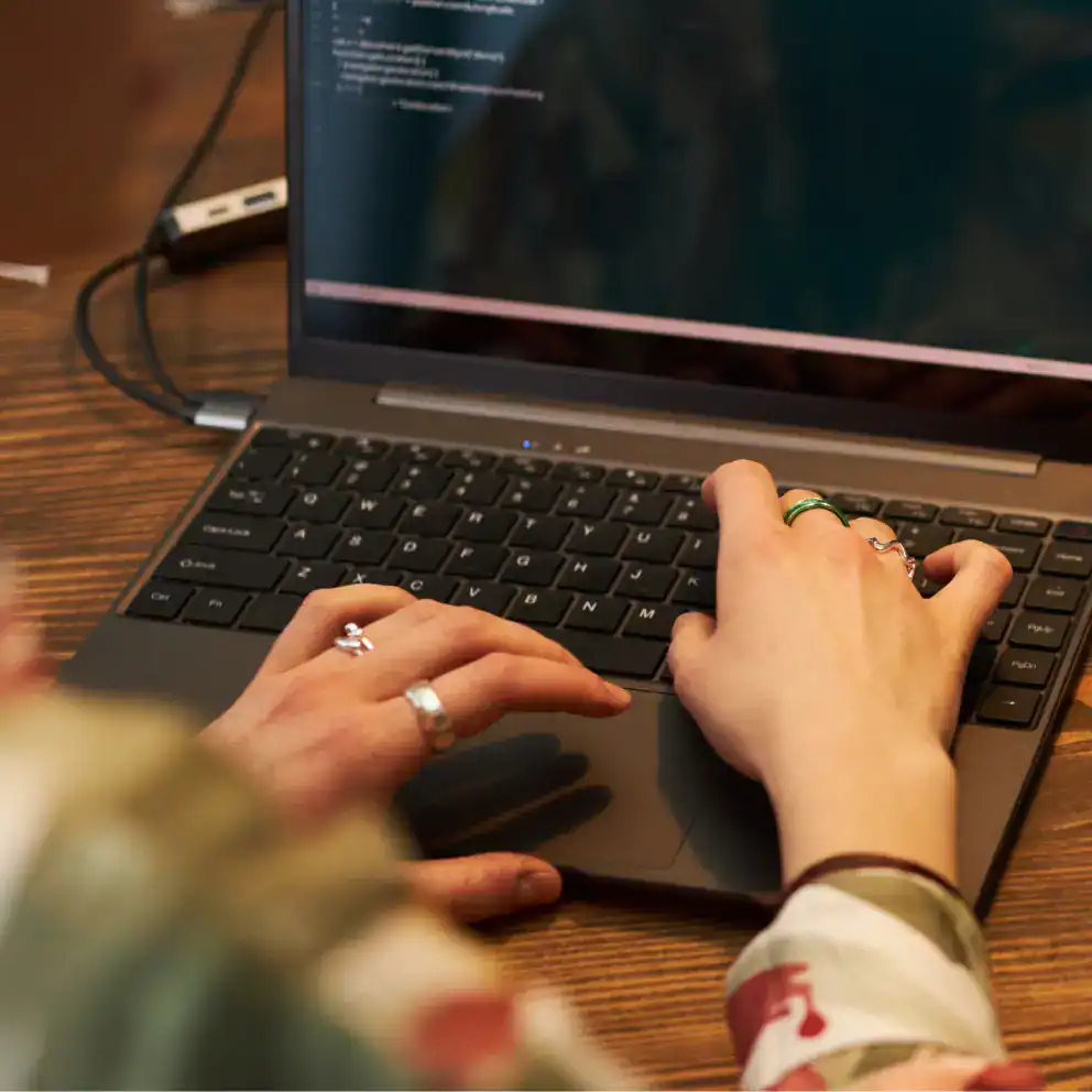 Person typing on a laptop with code displayed on the screen; their hands are visible on the keyboard, and a USB drive is plugged into the laptop.