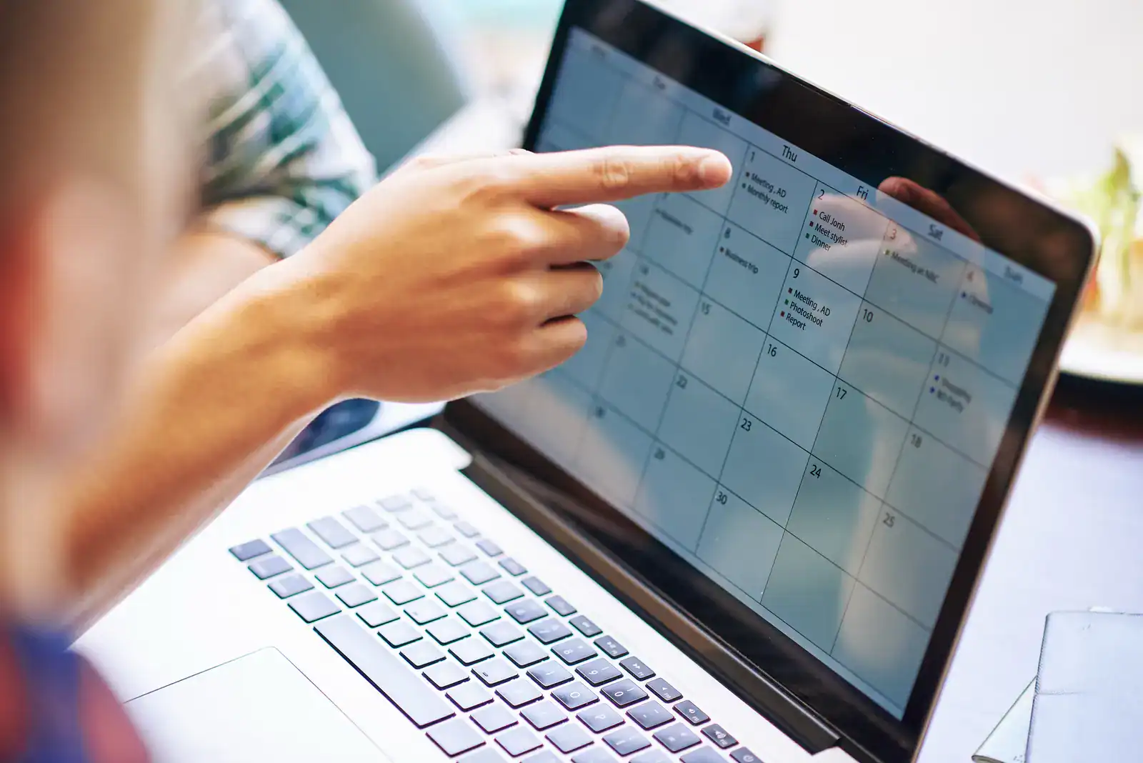 A person points at a digital calendar displayed on a laptop screen while another person looks on.